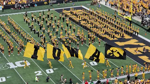 Iowa marching band and flag runners on the field during a football pregame