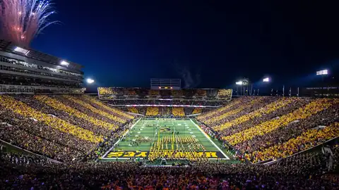 Packed Iowa football stadium under the lights with fireworks overhead