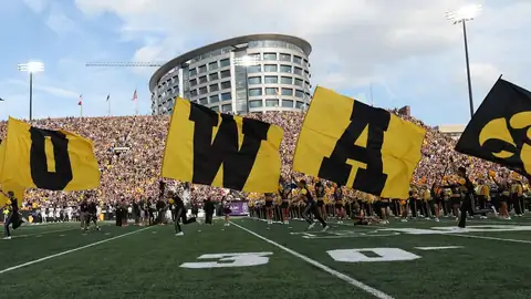 Iowa flag runners carrying I-O-W-A flags across the football field on gameday