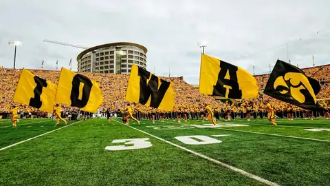 Iowa flag runners with I-O-W-A flags on the field in front of the stands