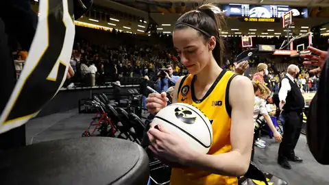 Iowa women's basketball player signing a basketball courtside for fans