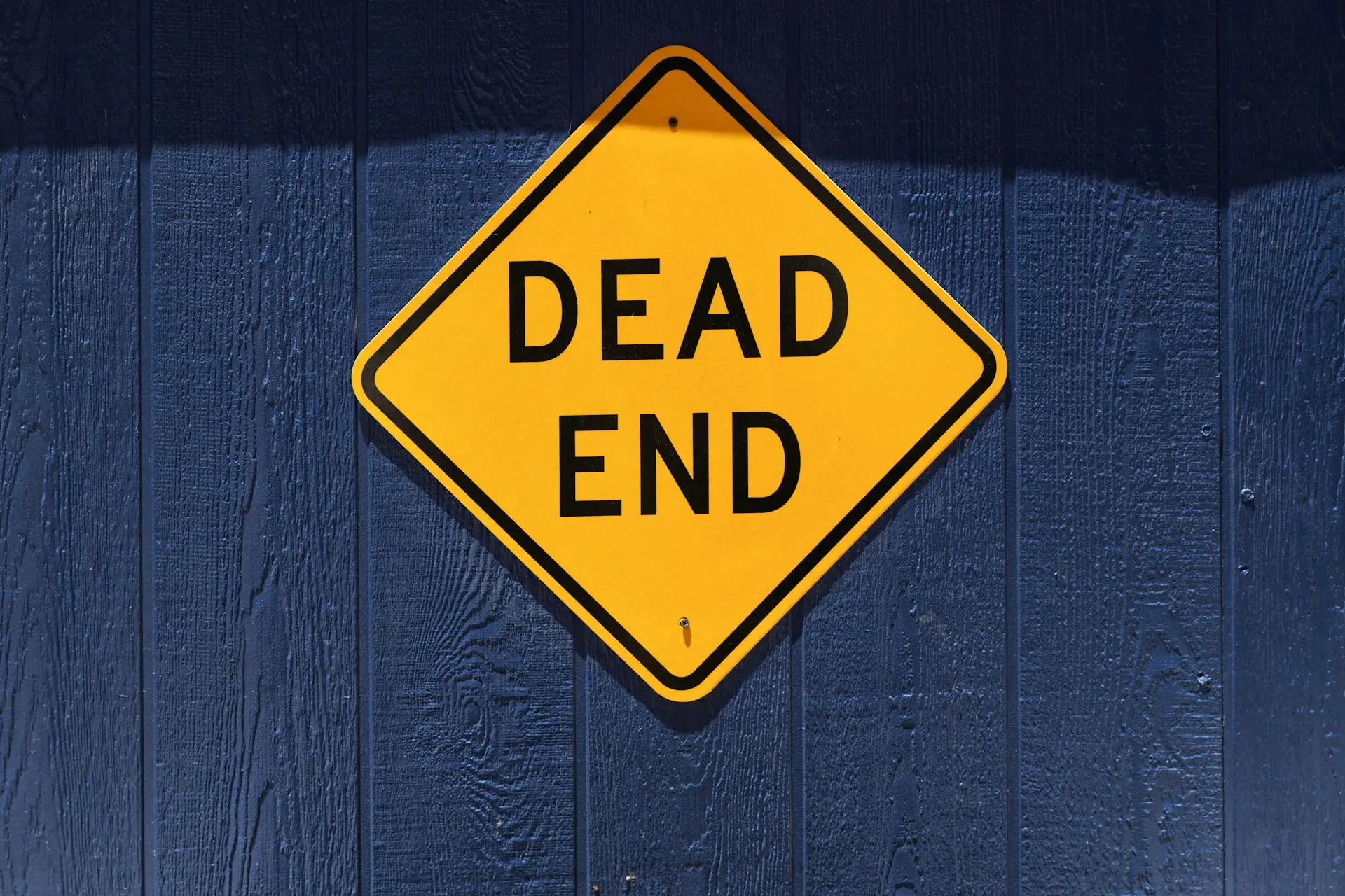 Yellow diamond-shaped Dead End road sign mounted on a dark blue wooden wall
