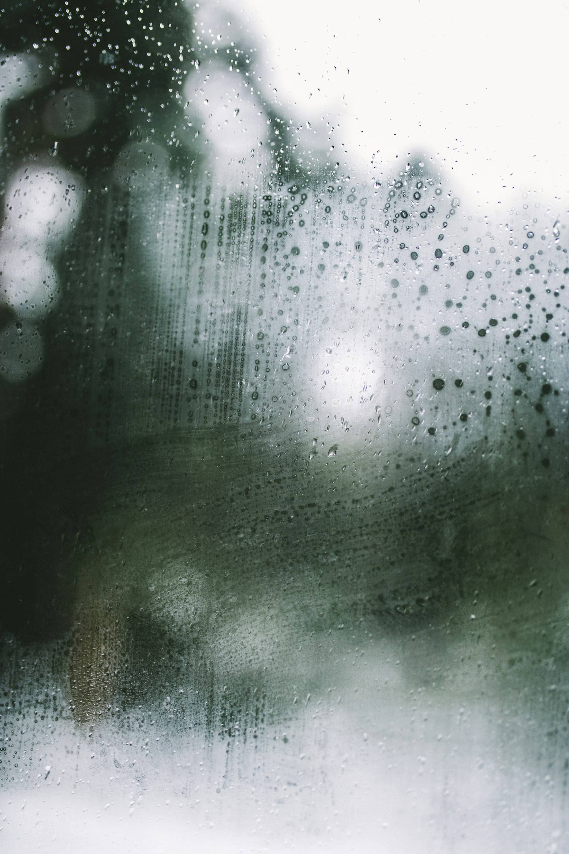 Rain-streaked window glass covered in condensation, blurring everything visible beyond it